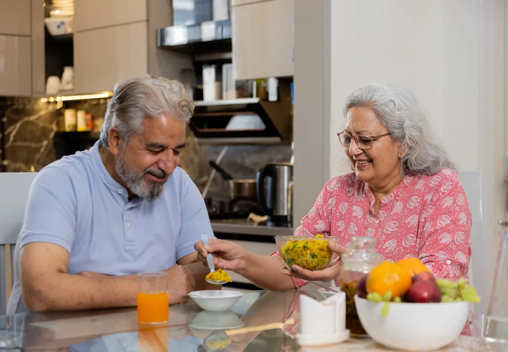 Happy retired senior indian couple eating healthy breakfast together, Elderly husband wife enjoy food at table, Love and bonding. Retirement life.