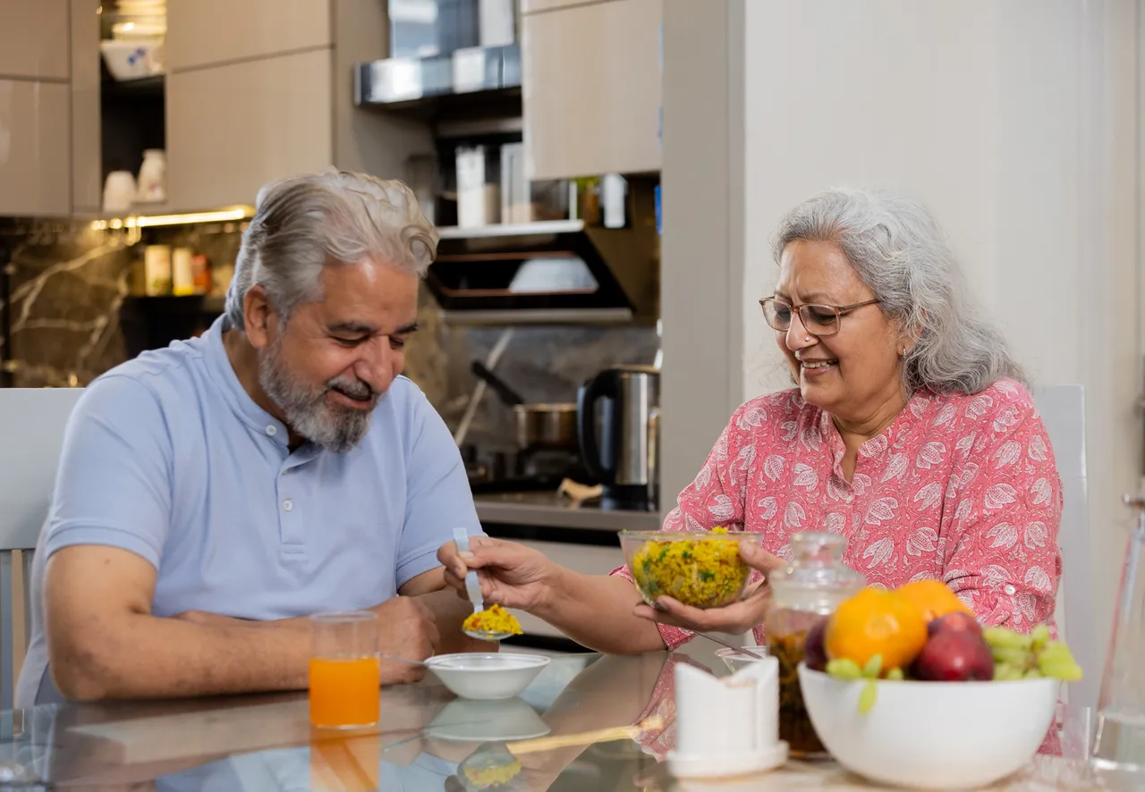 Happy retired senior indian couple eating healthy breakfast together, Elderly husband wife enjoy food at table, Love and bonding. Retirement life.