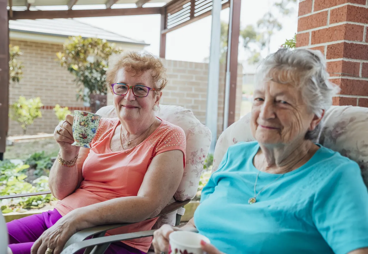 A shot of two senior friends laughing and enjoying a cup of tea together outside.