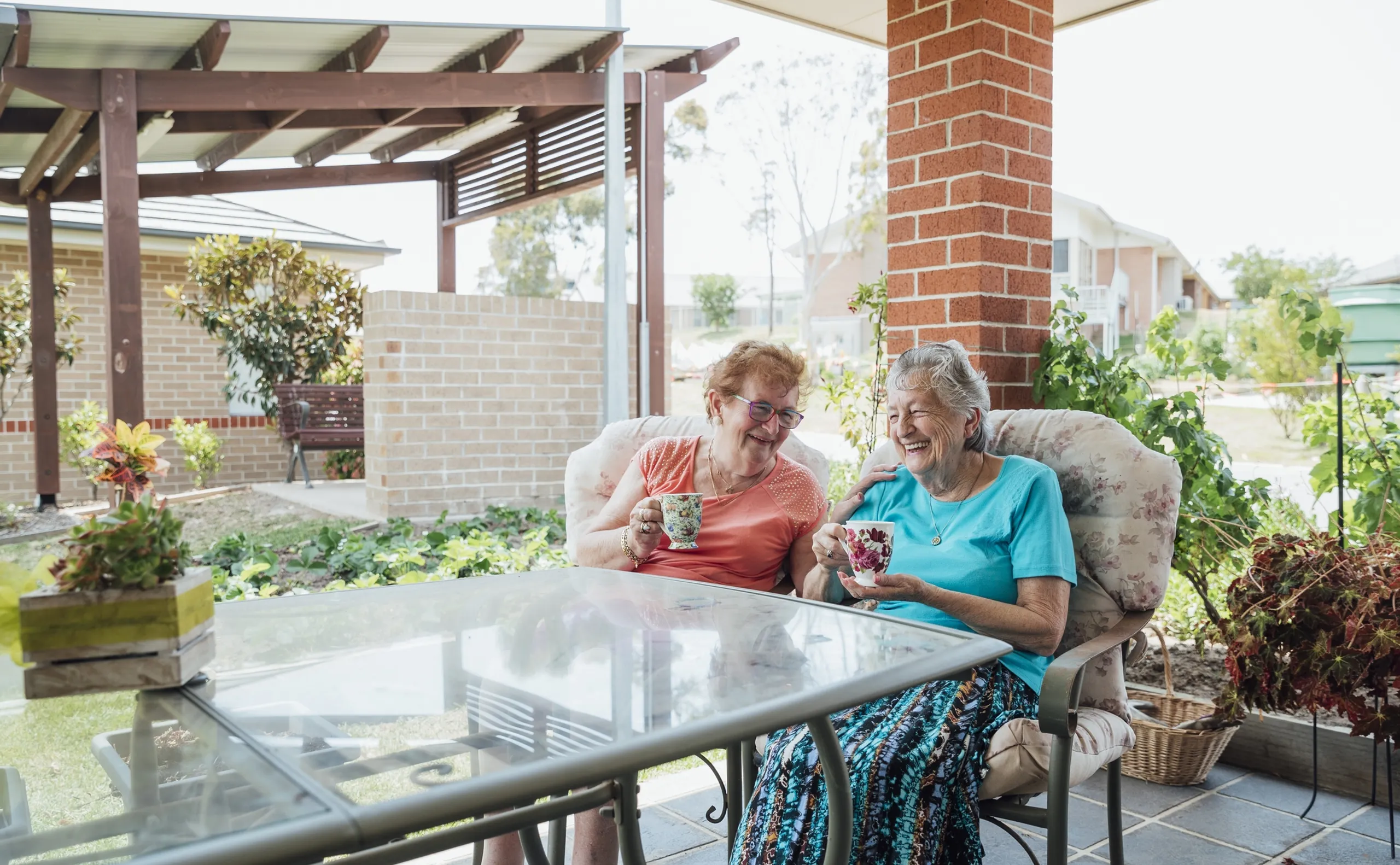 A shot of two senior friends laughing and enjoying a cup of tea together outside.