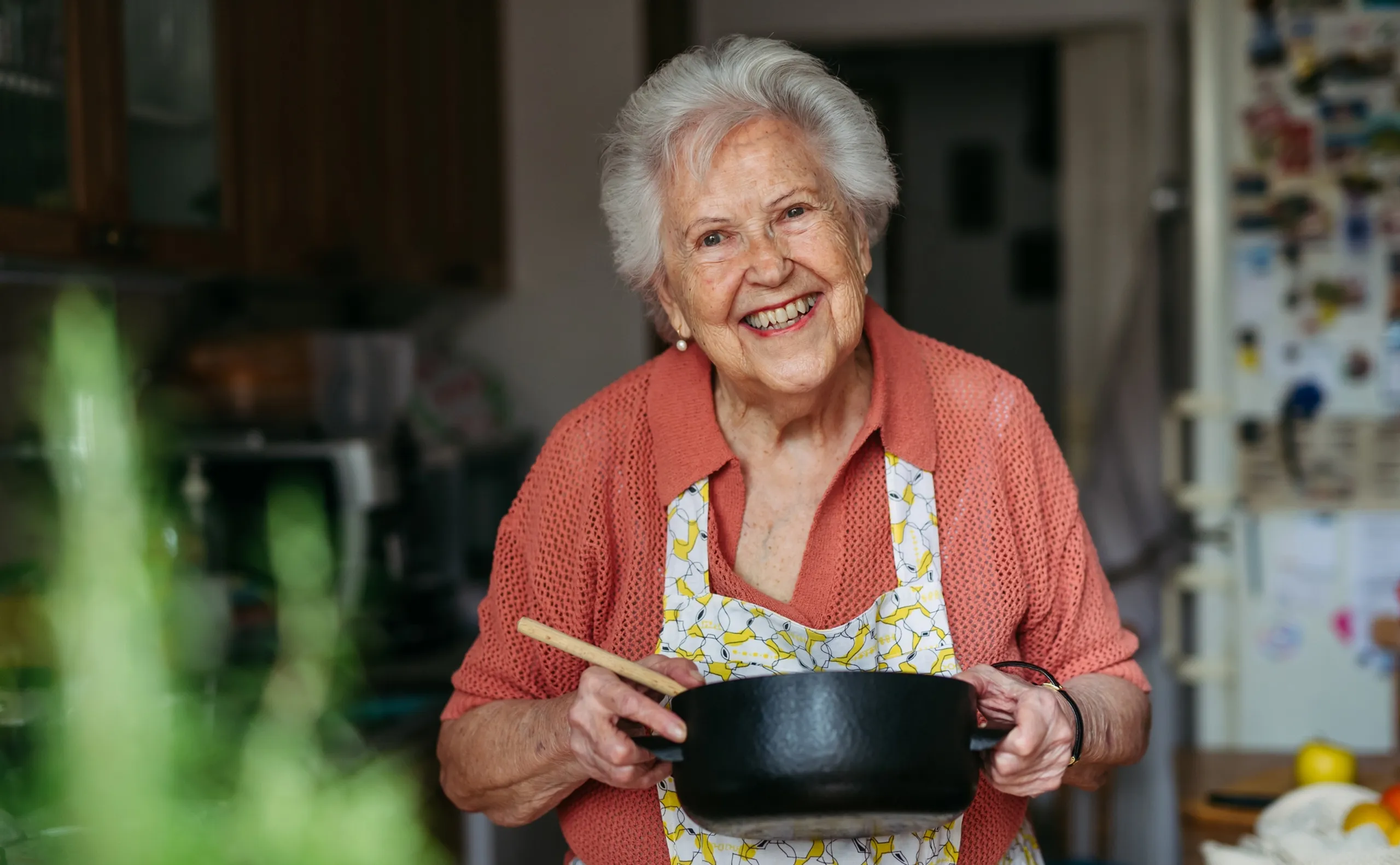 Happy senior woman cooking at home in kitchen.